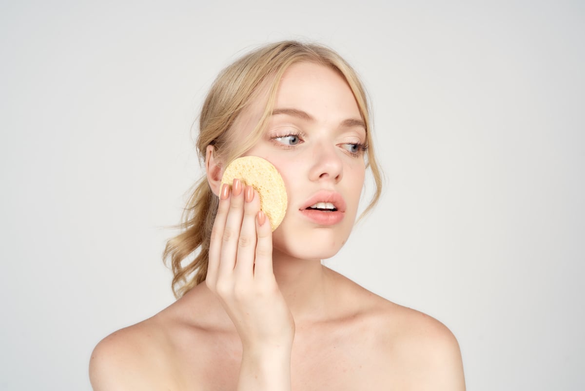 A Blonde with Bare Shoulders Holds Cotton Pads near Her Face Skin Care Light Background